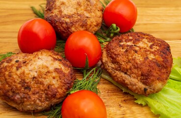 Fried chicken cutlets with vegetables on a wooden background. Meat balls with tomatoes and herbs on a wooden board.
