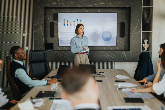 A diverse group of business people engaged in a meeting with a presentation displayed on a screen. The setting emphasizes collaboration and teamwork in a modern office environment. - Powered by Adobe