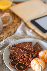 Books, e-reader, tea, orange juice, fruit, snacks, yarn, blanket and lit candles on the table. Autumn or winter hygge at home. Selective focus.