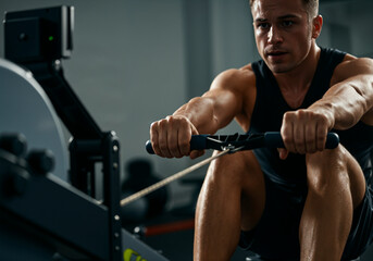 Muscular sportsman engaging in an intense workout session on a rowing machine in a modern gym, showcasing dedication and focus