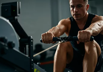 Muscular sportsman engaging in an intense workout session on a rowing machine in a modern gym, showcasing dedication and focus