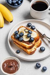 Toasted bread with chocolate cream, blueberries and banana on a plate on a light background