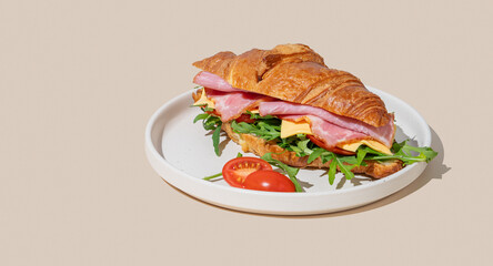 Croissant sandwich with ham, cheese and arugula on a plate on a yellow background with a shadow.
