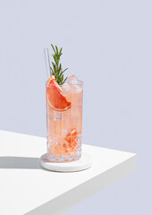 Refreshing cocktail with grapefruit, rosemary and ice in a glass on a blue background with shadow.