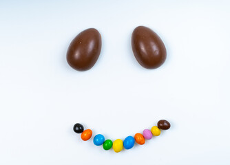 Chocolate eggs bring smiles!. Chocolate eggs form eyes while colorful candies shape a smile on a white background, creating a cheerful display.