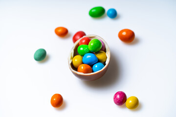 Candy egg on white background. A decorative egg filled with vibrant candies sits surrounded by more colorful treats on a clean, white surface.