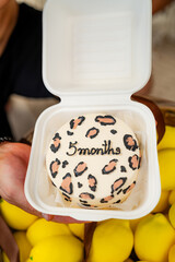 5 months of leopard print fun!. A person holds a container showcasing a decorated cake celebrating five months, adorned with a leopard pattern.