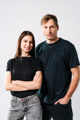 Fototapeta premium Casual portrait of a couple. Young couple standing together in casual black outfits, smiling confidently against a plain white background.