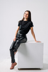 Young woman poses stylishly on a cube. A woman wearing black attire sits confidently on a white...
