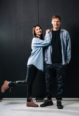 Couple posing together in studio setting. Two individuals are standing together in a studio, showcasing casual yet stylish attire, with an elegant backdrop.