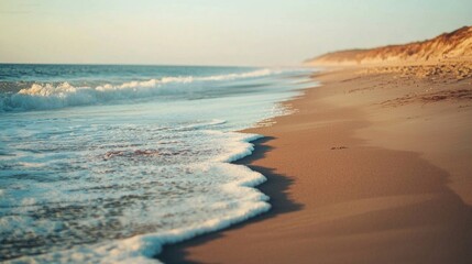 Fototapeta premium As the sun descends, warm golden rays shimmer across the gentle waves rolling onto the shore. The beach embraces serenity with soft sands and distant cliffs