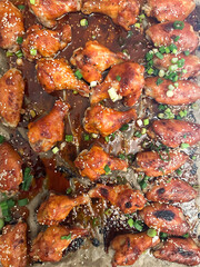 Top view of baked chicken wings glazed in sweet and spicy sauce, garnished with sesame seeds and chopped green onions on parchment paper.