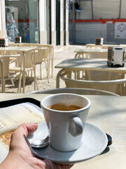 Espresso cup on a saucer with a spoon, hand holding the cup, outdoor café setting