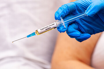 The picture shows a doctor holding a syringe with the typhoid fever vaccine in her hand, wearing...