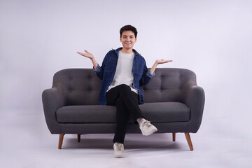 Full body image of young Asian man posing on sofa on white background