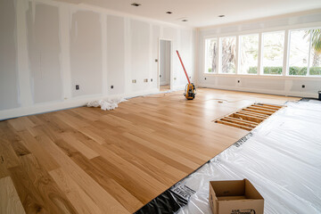 A spacious, unfinished living room with wooden flooring installation in progress.