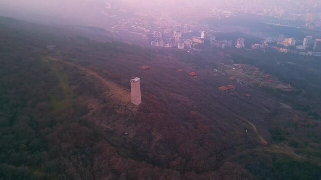 Ancient Georgian tower against the backdrop of modern Tbilisi city at dusk.