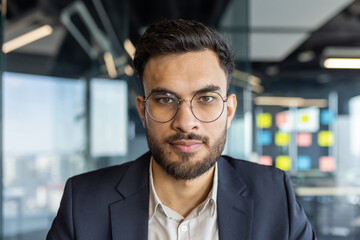 Close-up portrait of a calm serious businessman in a business suit. Man looking at the camera, at his workplace inside the office.