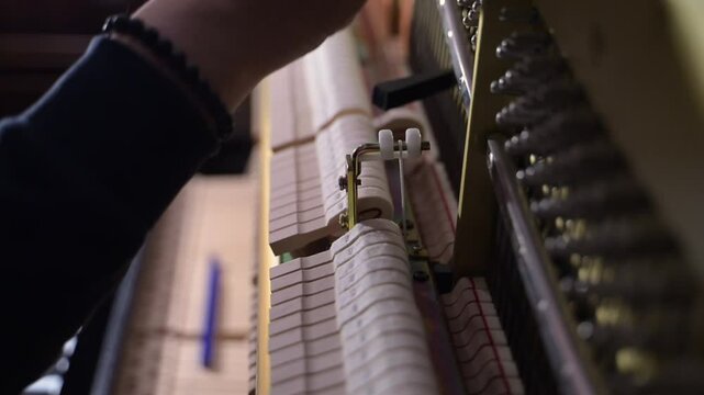 Technician tuning an upright piano  and using lever and tools to tighten or loosen the strings to produce proper musical pitch.