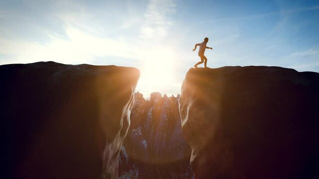 Courageous man jumping over a gap on a mountain peak at sunrise.