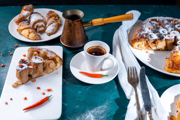 A slice of banana pie with hot chili peppers and coffee cooked in a cezve on a dark green background. French Tarte Tatin and handmade croissants on the table.