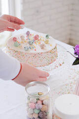 cropped shot of woman decorating Easter cake with sweet eggs in the kitchen