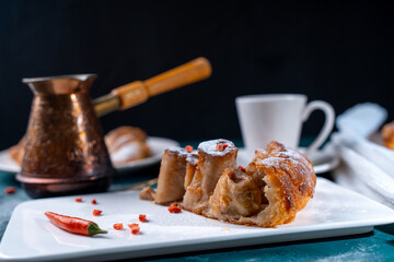 A slice of banana pie with hot chili peppers and coffee cooked in a cezve on a dark green background. French Tarte Tatin and handmade croissants on the table.