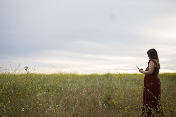 Shot of a woman using a cellphone in a field. Lady holding a smartphone looking sideways. Horizontal
