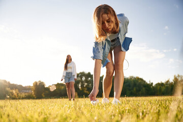 Picking up the fallen shuttlecock. Two women are having fun, with badminton rackets, on the field