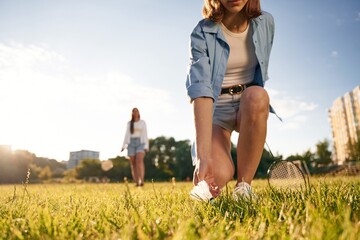 Picking up the fallen shuttlecock. Two women are having fun, with badminton rackets, on the field