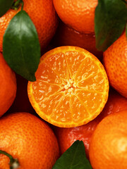 Сlose-up of a tangerine cut. Half a tangerine lies on a group of tangerines with green leaves. Top view. Juicy citrus pulp full of vitamin C