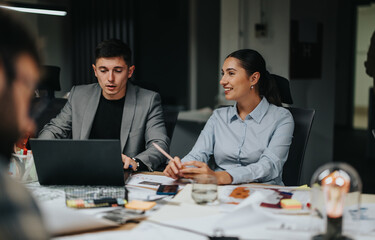 A group of people engaged in brainstorming and analysis during a late-night office meeting. They...