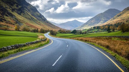 Naklejka premium Countryside roads nature concept. A winding road through majestic mountains and lush green fields under a cloudy sky.
