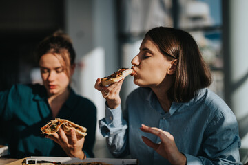 Two women savor a delicious pizza, enjoying a relaxed lunch break together. The scene captures the...