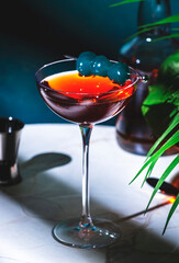 Rob Roy alcoholic cocktail drink with scotch whiskey, sweet vermouth, bitters and cherry. Marble table, blue background with tropical leaves