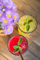 Top view summer lemonades in glasses with ice and mint on wooden table