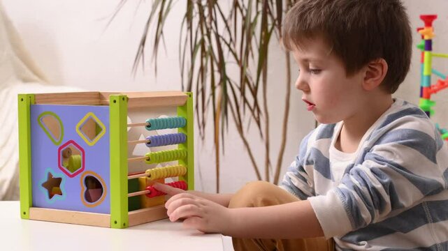 5 year old boy learning to count on colored wooden abacus. Child development and preschool education. kindergarten. Educational games for toddlers. World Autism Awareness Day	