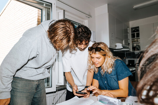 Male and female students sharing smart phone while studying together in college dorm