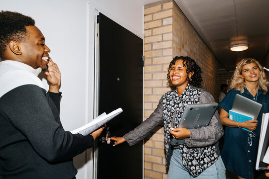 Happy male and female students laughing while standing in corridor