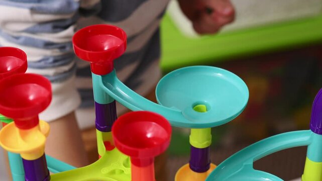Hand closeup of boy plays with little balls in multi-colored construction set, a labyrinth for balls. Development of logic and fine motor skills in preschool children. Independent play