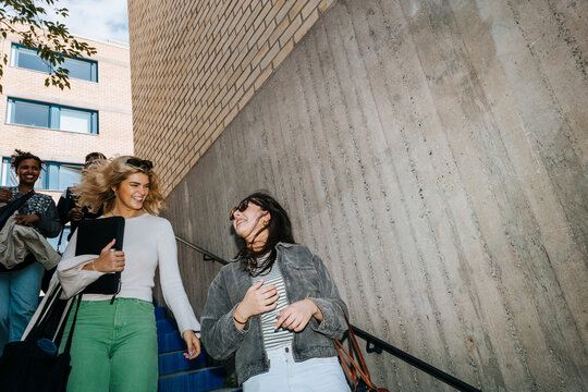 Low angle view of happy female students talking while moving down from stairs