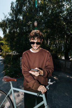 Smiling young man using smart phone while standing with bicycle at park