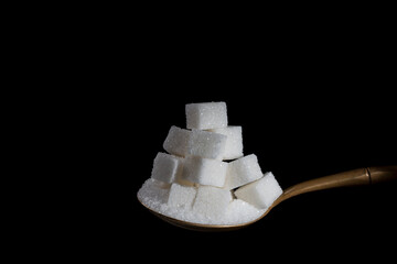 White cubes sugar and granulated sugar in spoon on black background, closeup. The concept of unhealthy eating, obesity, heart disease, diabetes