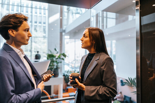 Businesswoman holding coffee cup and discussing with male colleague while standing in elevator - Powered by Adobe