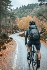 Obraz premium A lone cyclist rides along a winding road surrounded by vibrant autumn trees and a serene forest backdrop, capturing the essence of outdoor adventure