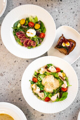 A beautifully arranged gourmet meal featuring two vibrant salads with fresh greens, cherry tomatoes, and gourmet protein, served on a textured table. Perfect for showcasing healthy dining options.