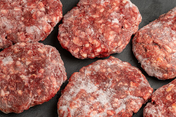 Close-up of several frozen hamburger patties on a dark surface. Ready for grilling or cooking....