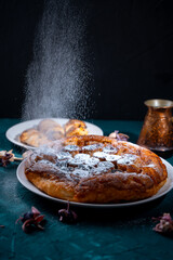Banana Tarte Tatin is sprinkled with powdered sugar on a white plate on a dark background. The powder is poured onto the cake. Vertical Photo