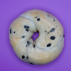 A close-up photo of a blueberry bagel, showing its chewy texture and juicy blueberries. contrasts with the purple background. Perfect for a break.