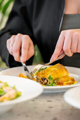 A close-up of a person using a fork and knife to cut into a delicious omelette on a plate. Fresh salads and a bowl of soup are visible in the background, highlighting a cozy dining experience.